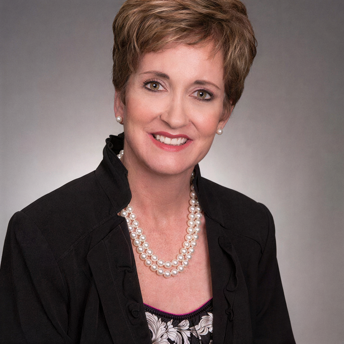 Headshot of Elisa Medhus, M.D., founder of VitalithMD®, wearing a black jacket and pearl necklace, smiling, with short light brown hair.